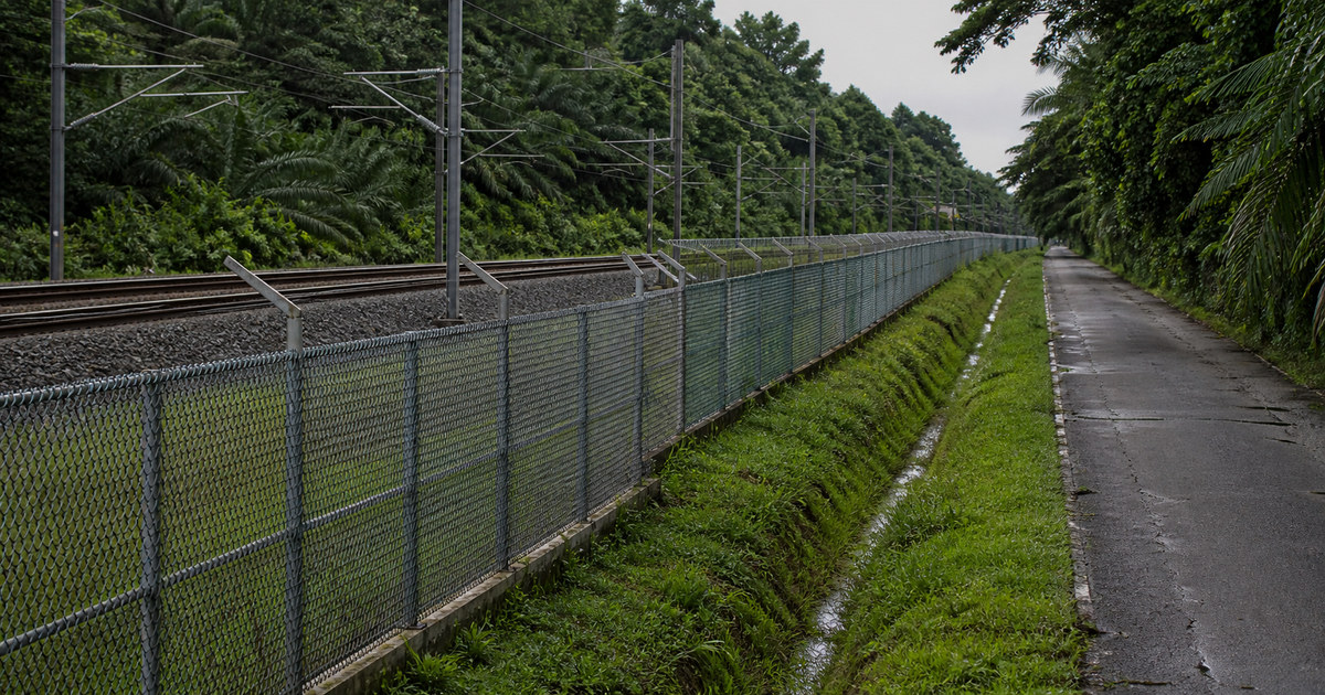Fenced railway corridor separated from an industrial service road in Serendah